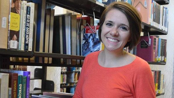 Woman in orange shirt standing in front of library book shelves